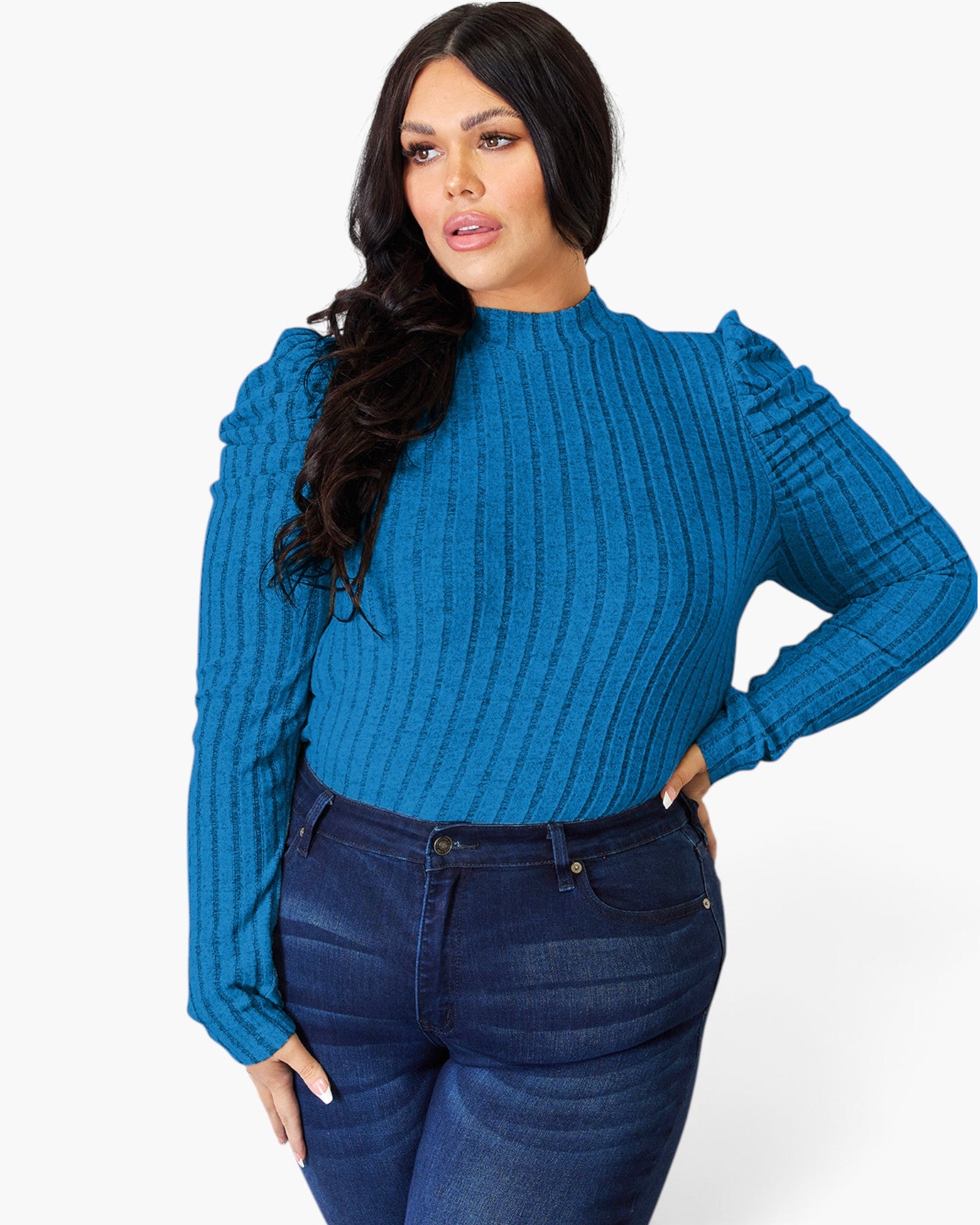 A woman modeling a bright blue ribbed knit mock-neck sweater with puffed long sleeves, paired with dark blue jeans, against a plain white studio background.