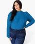 A woman modeling a bright blue ribbed knit mock-neck sweater with puffed long sleeves, paired with dark blue jeans, against a plain white studio background.