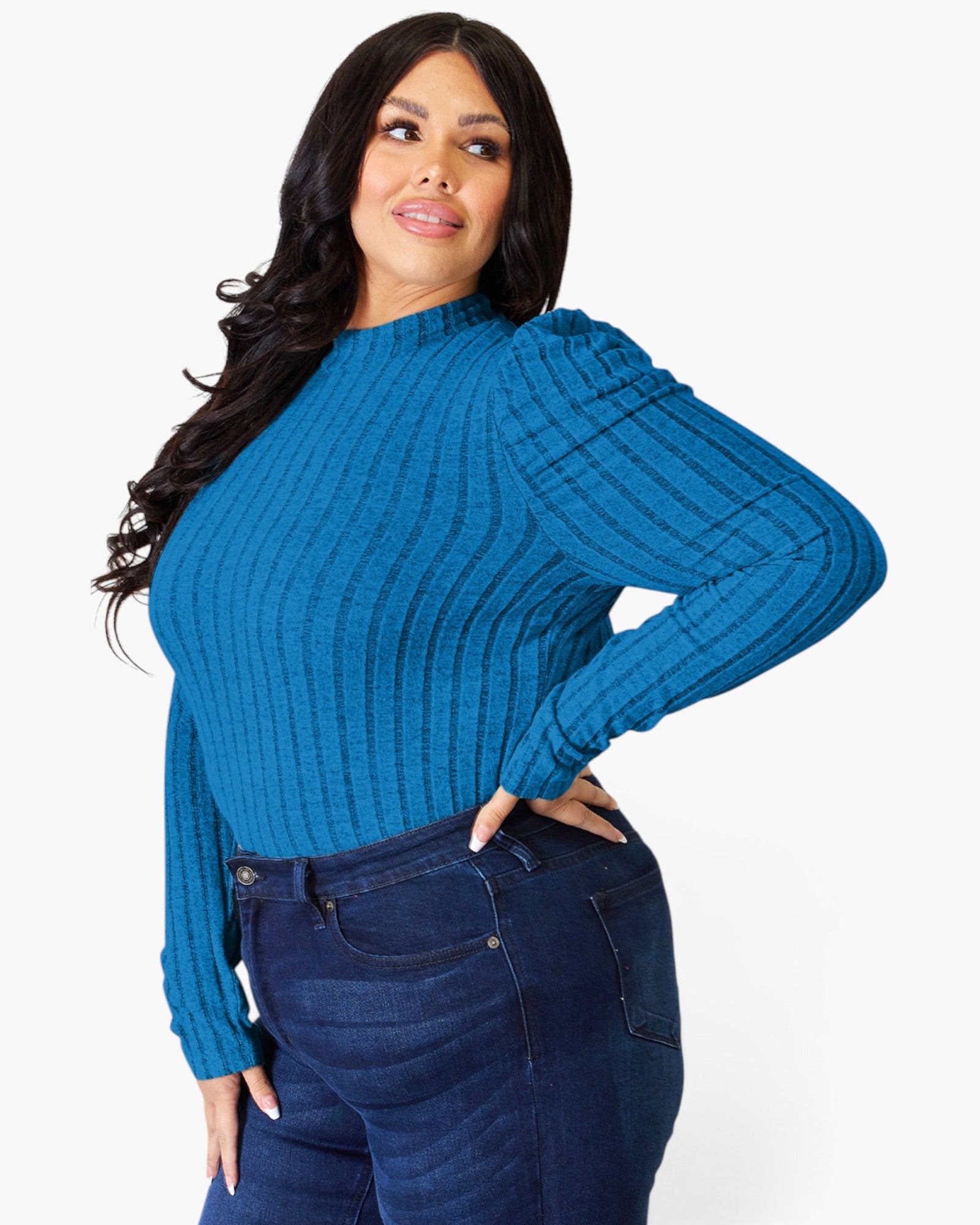 A woman modeling a bright blue ribbed long-sleeve mock neck sweater paired with dark blue jeans, set against a plain light gray background.