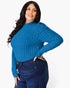 A woman modeling a bright blue ribbed long-sleeve mock neck sweater paired with dark blue jeans, set against a plain light gray background.
