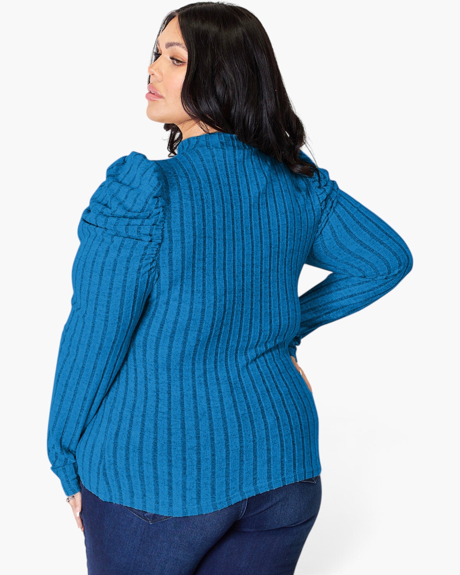 A woman shown from the back wearing a bright blue ribbed knit sweater with dramatic puffed shoulders, paired with dark blue jeans, against a plain light gray studio background.