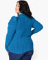 A woman shown from the back wearing a bright blue ribbed knit sweater with dramatic puffed shoulders, paired with dark blue jeans, against a plain light gray studio background.