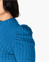 Close-up of a person wearing a textured blue ribbed top with puffed shoulders against a plain light background.