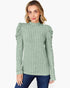 A woman wearing a sage green ribbed knit mock neck sweater with dramatic puffed sleeves, paired with dark blue jeans, against a plain white background.