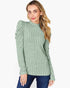 A woman wearing a sage green ribbed knit mock-neck sweater with puffed sleeves, paired with dark blue jeans, against a plain white background.