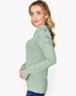 A woman wearing a sage green ribbed knit mock neck sweater, shown from a side profile against a plain white background.