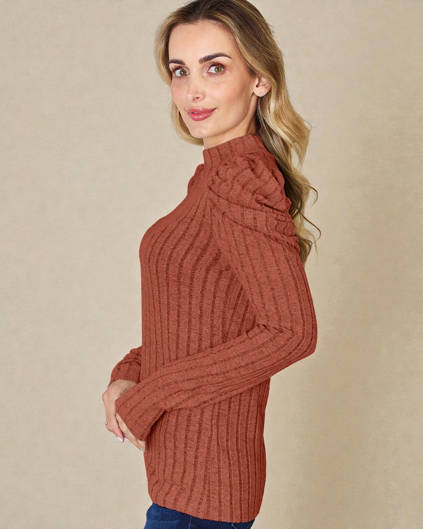 Woman wearing a rust-colored ribbed sweater against a beige background