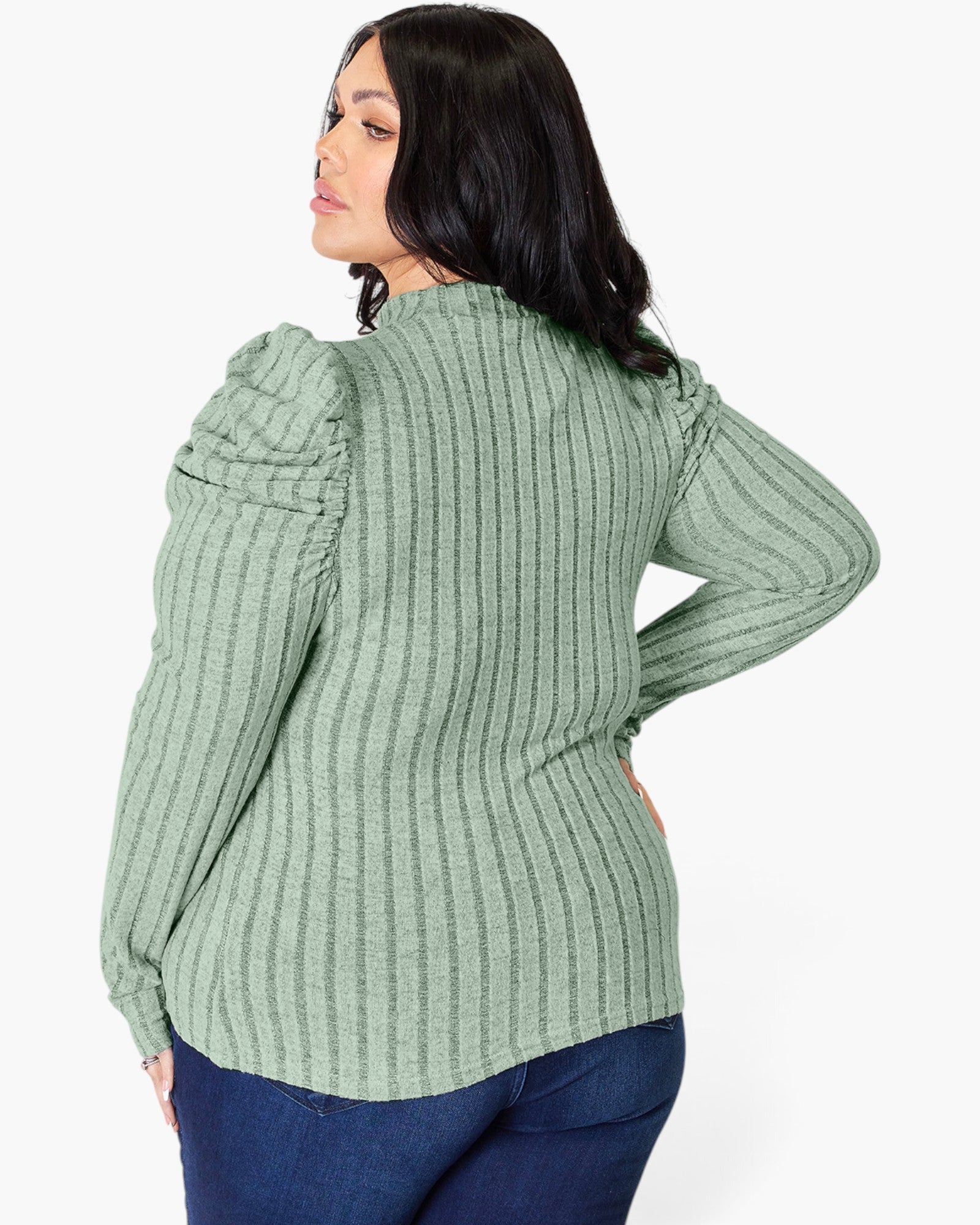 A woman shown from the back wearing a sage green ribbed knit top with puffed shoulders and dark blue jeans, against a plain light gray background.