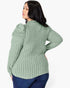 A woman shown from the back wearing a sage green ribbed knit top with puffed shoulders and dark blue jeans, against a plain light gray background.