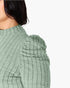 Close-up of a model wearing a sage green ribbed knit top with puffed shoulders against a plain white background.