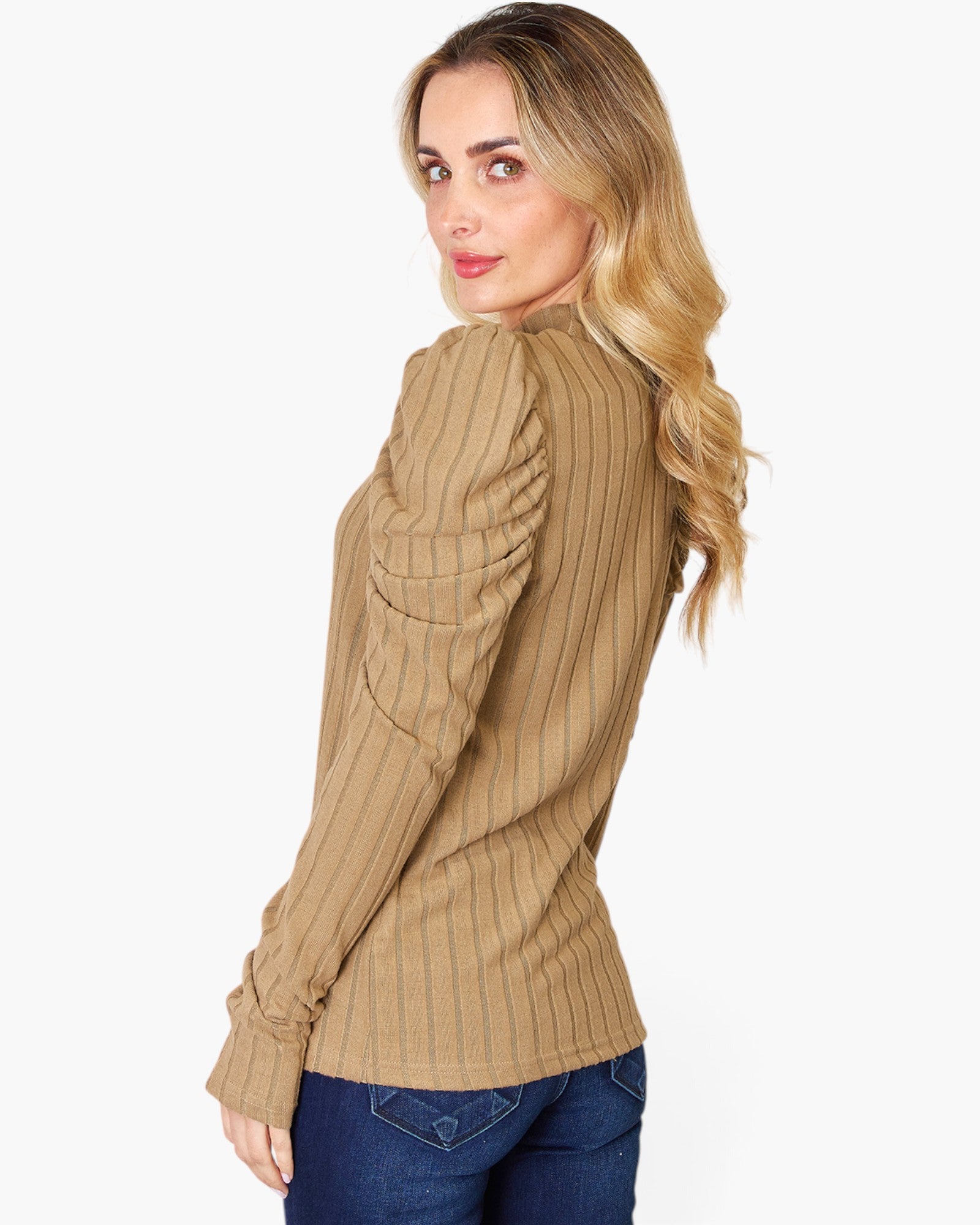 A woman with blonde hair is shown from a side-back angle wearing a tan ribbed long-sleeve top and blue jeans against a plain white background.