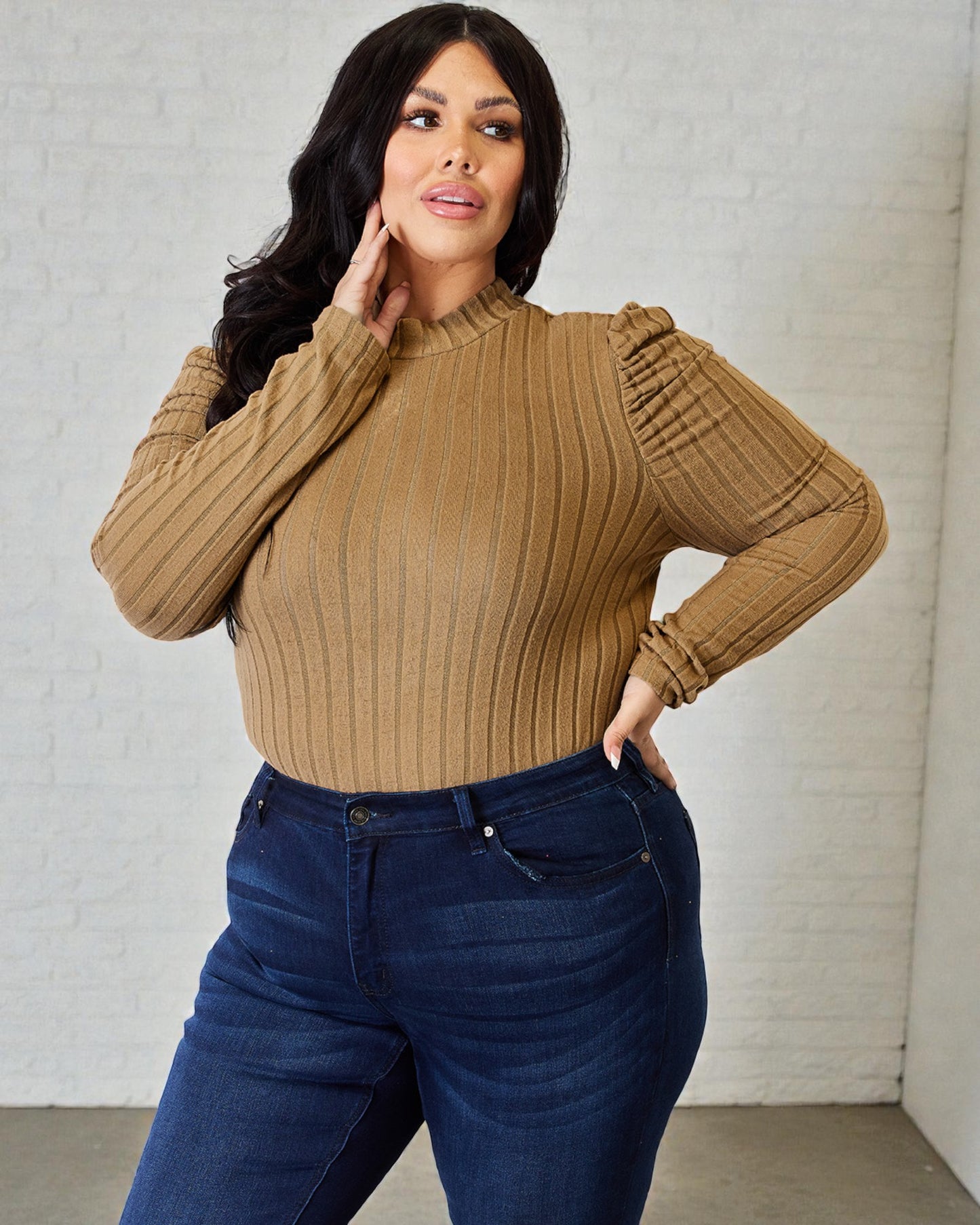 Woman wearing a brown ribbed sweater and blue jeans against a light gray background