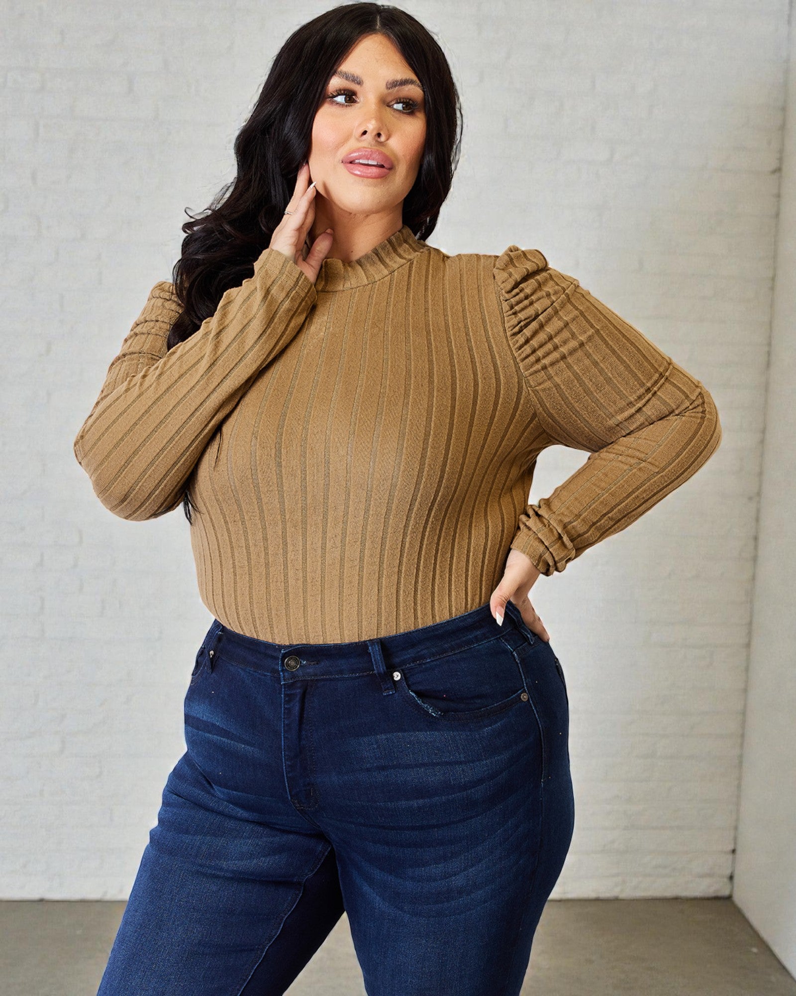Woman wearing a brown ribbed sweater and blue jeans against a light gray background