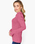 A woman wearing a pink ribbed knit mock neck sweater with shoulder detailing, paired with blue jeans, photographed against a solid white background.