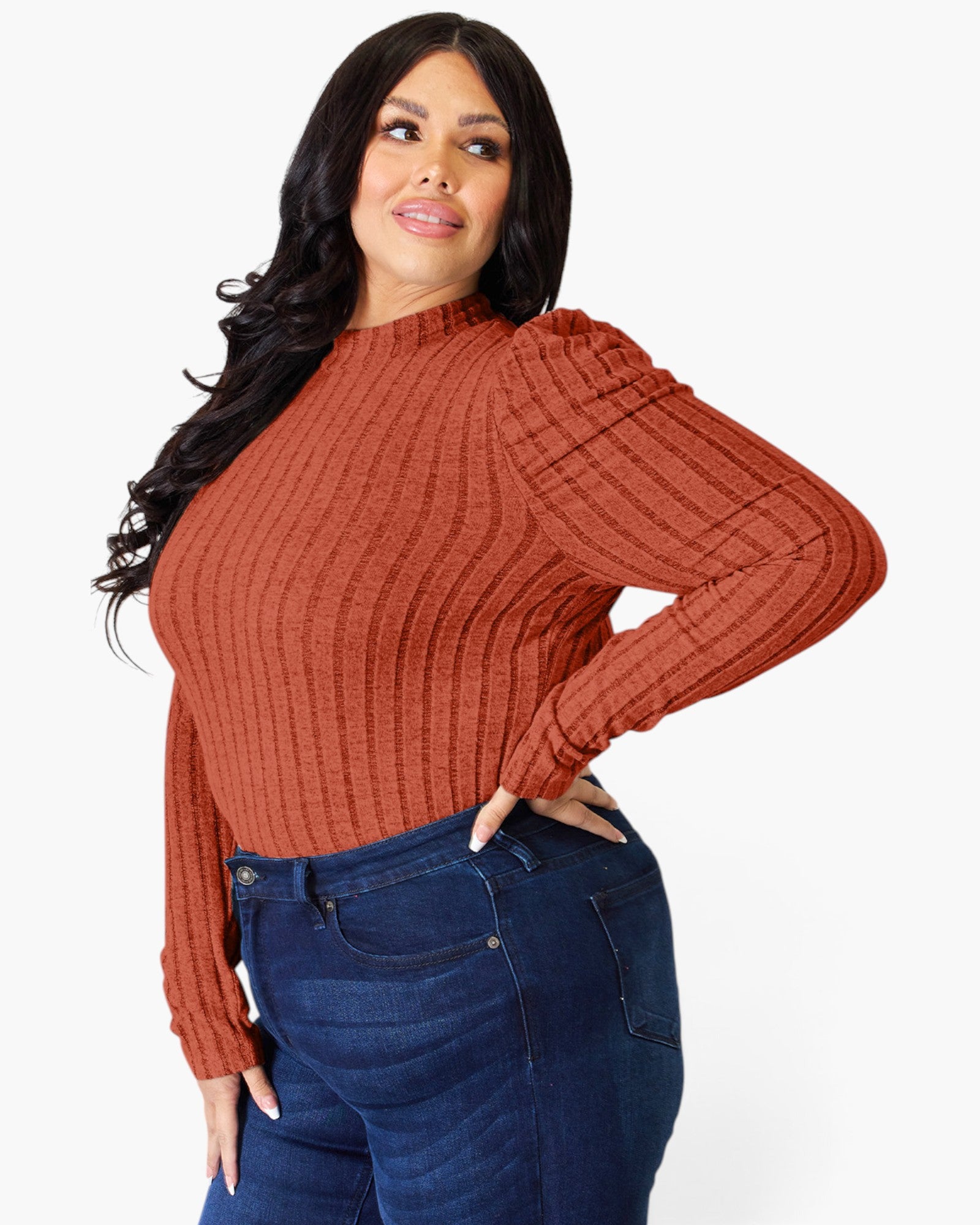 A woman modeling a ribbed long-sleeve mock neck sweater in a rust orange color, paired with dark blue jeans, against a plain white background.
