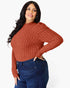 A woman modeling a ribbed long-sleeve mock neck sweater in a rust orange color, paired with dark blue jeans, against a plain white background.