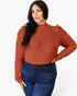 A woman modeling a ribbed long-sleeve mock neck top in a rust orange color, paired with dark blue jeans, against a plain white background.