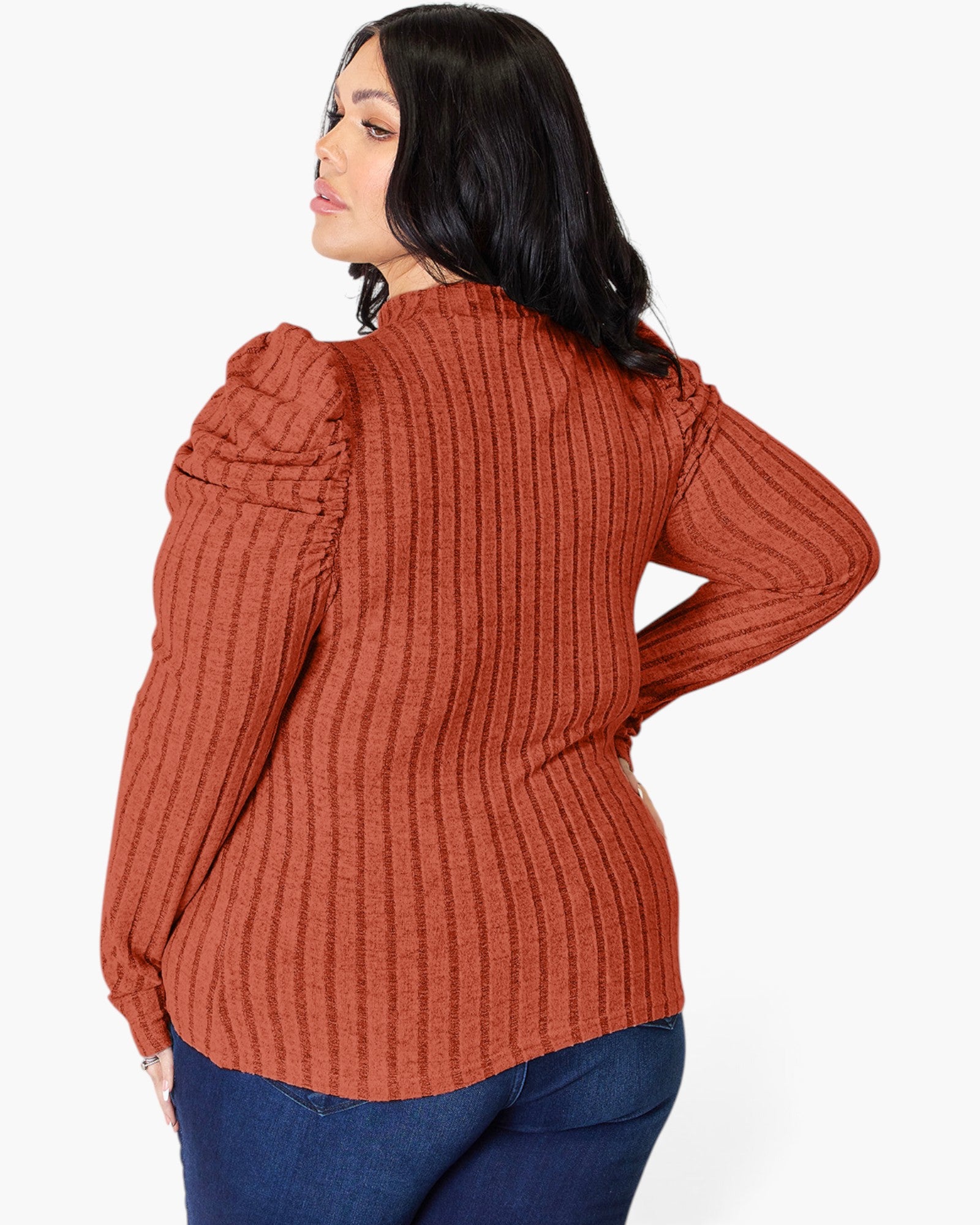 A woman wearing a rust-orange ribbed knit long-sleeve top with puffed shoulders, shown from the back against a light gray studio background.