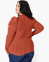 A woman wearing a rust-orange ribbed knit long-sleeve top with puffed shoulders, shown from the back against a light gray studio background.