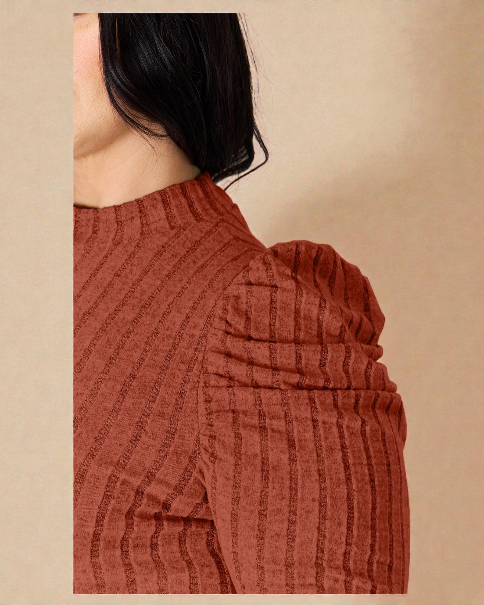Close-up of a person wearing a rust-colored ribbed sweater against a beige background
