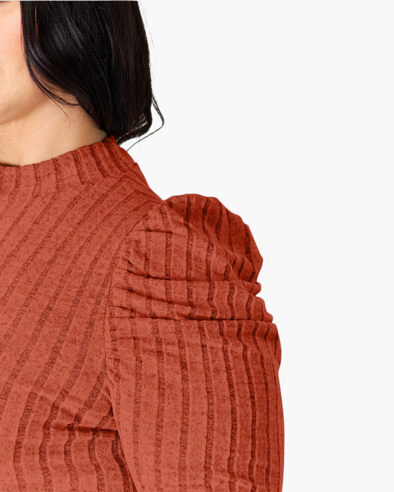 Close-up of a person wearing a ribbed knit top in a warm rust or terracotta color, showing the shoulder and side of the head against a plain light background.