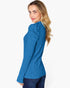 A woman wearing a bright blue ribbed knit sweater with a high ruffled collar, shown from a side-back angle against a plain white background.