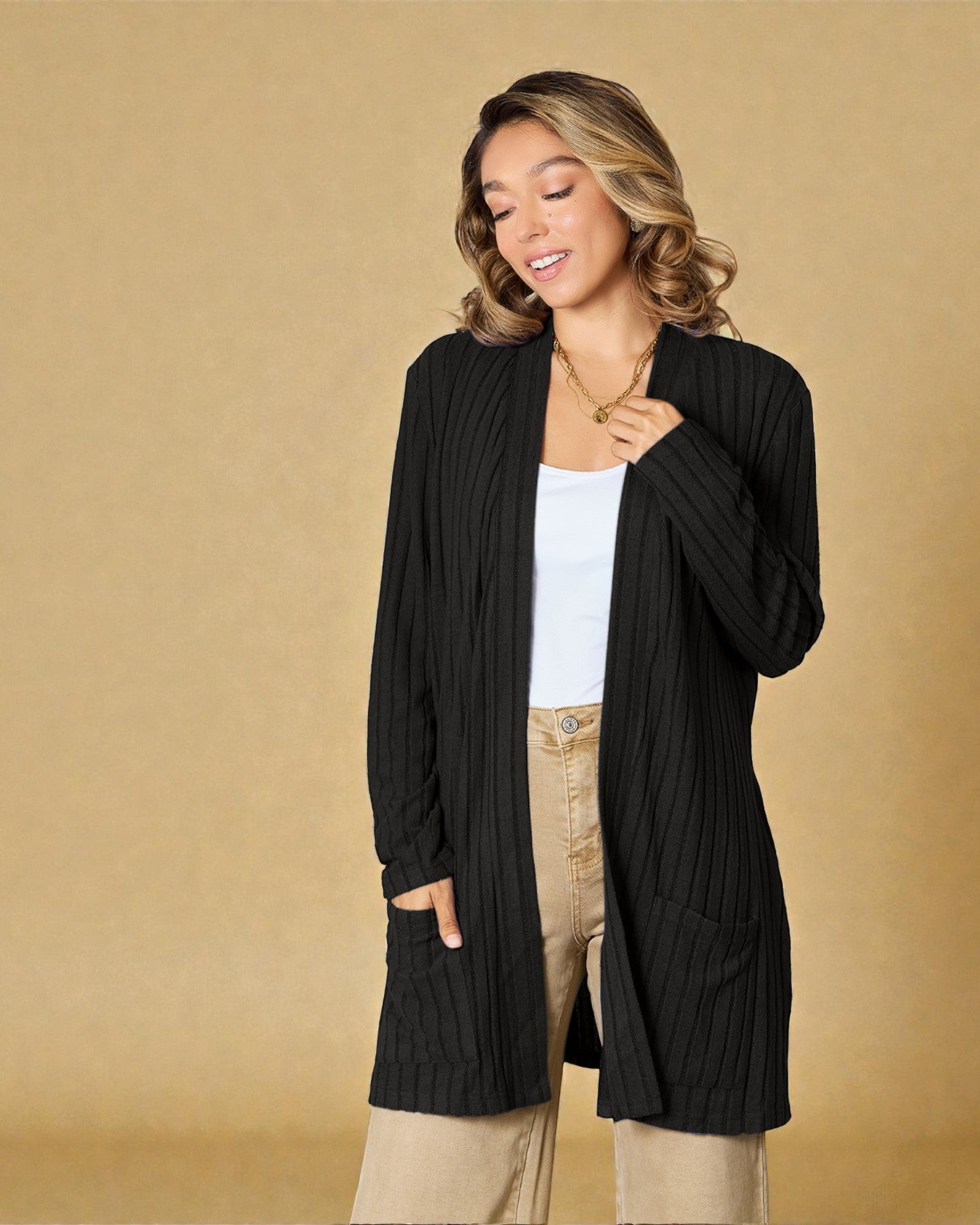 Woman wearing a black cardigan over a white top and beige pants on a beige background