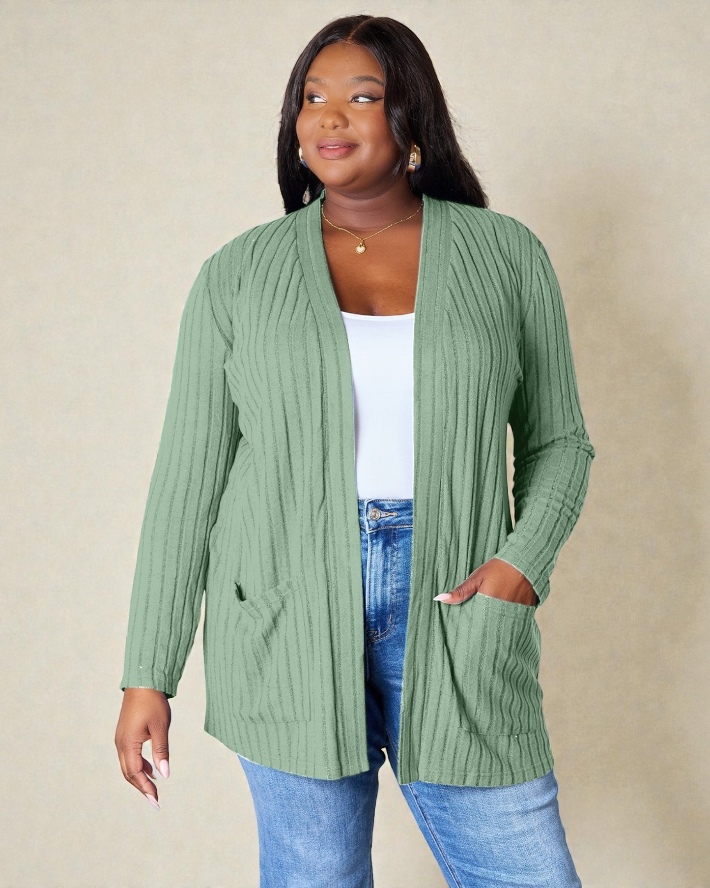 Woman wearing a green ribbed cardigan over a white top and blue jeans on a beige background