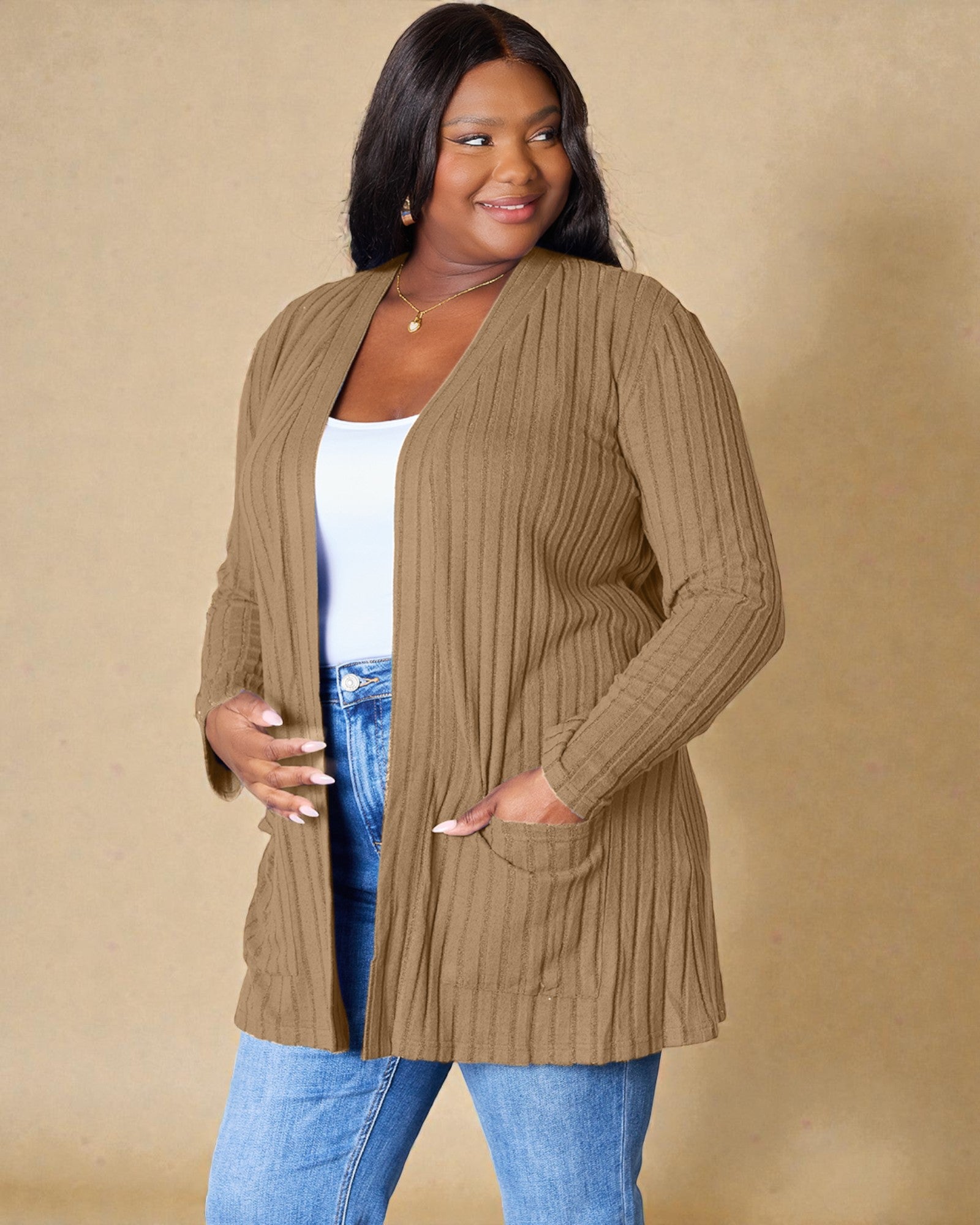 Woman wearing a brown ribbed cardigan over a white top and blue jeans on a beige background