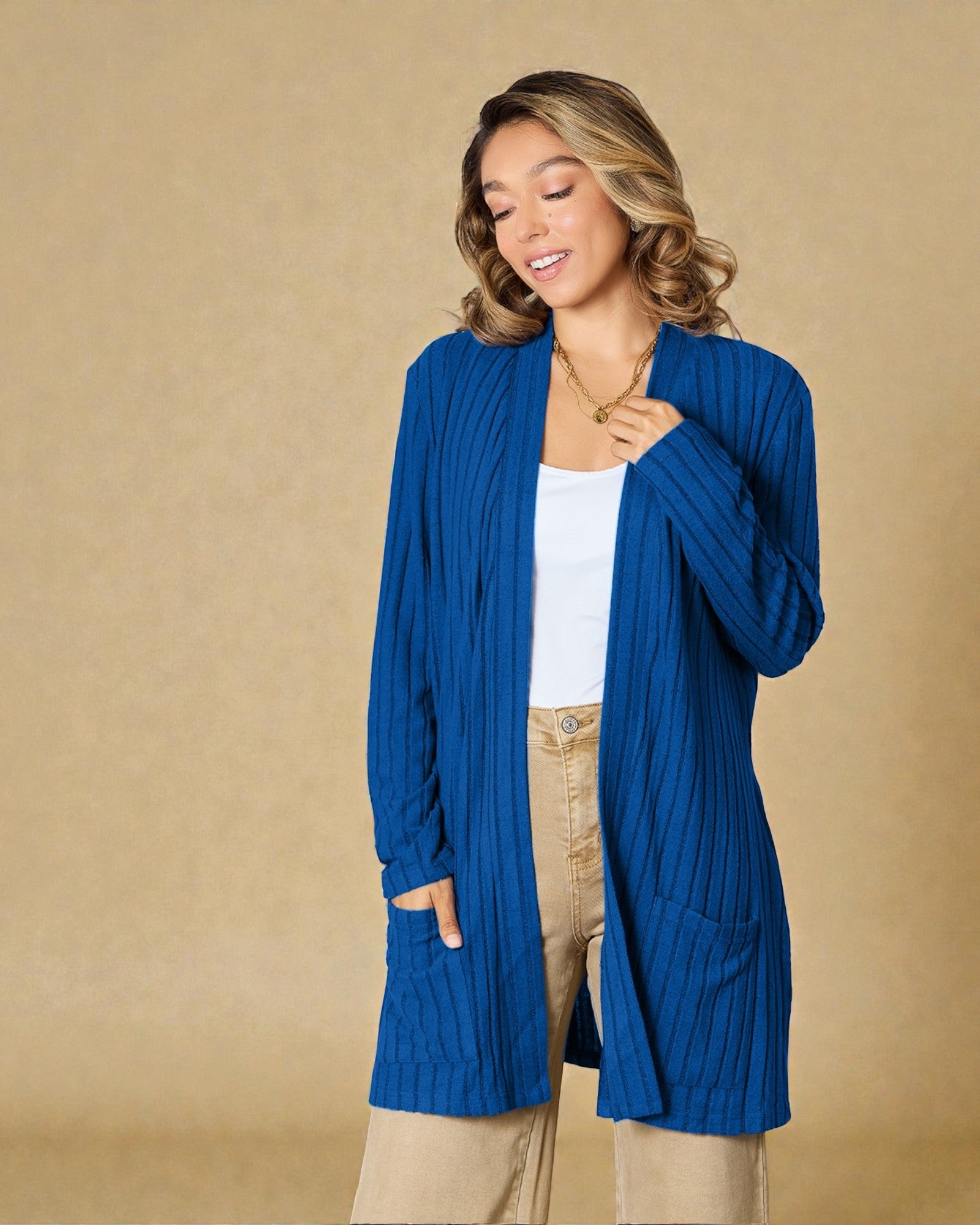 Woman wearing a blue cardigan over a white top and beige pants on a beige background