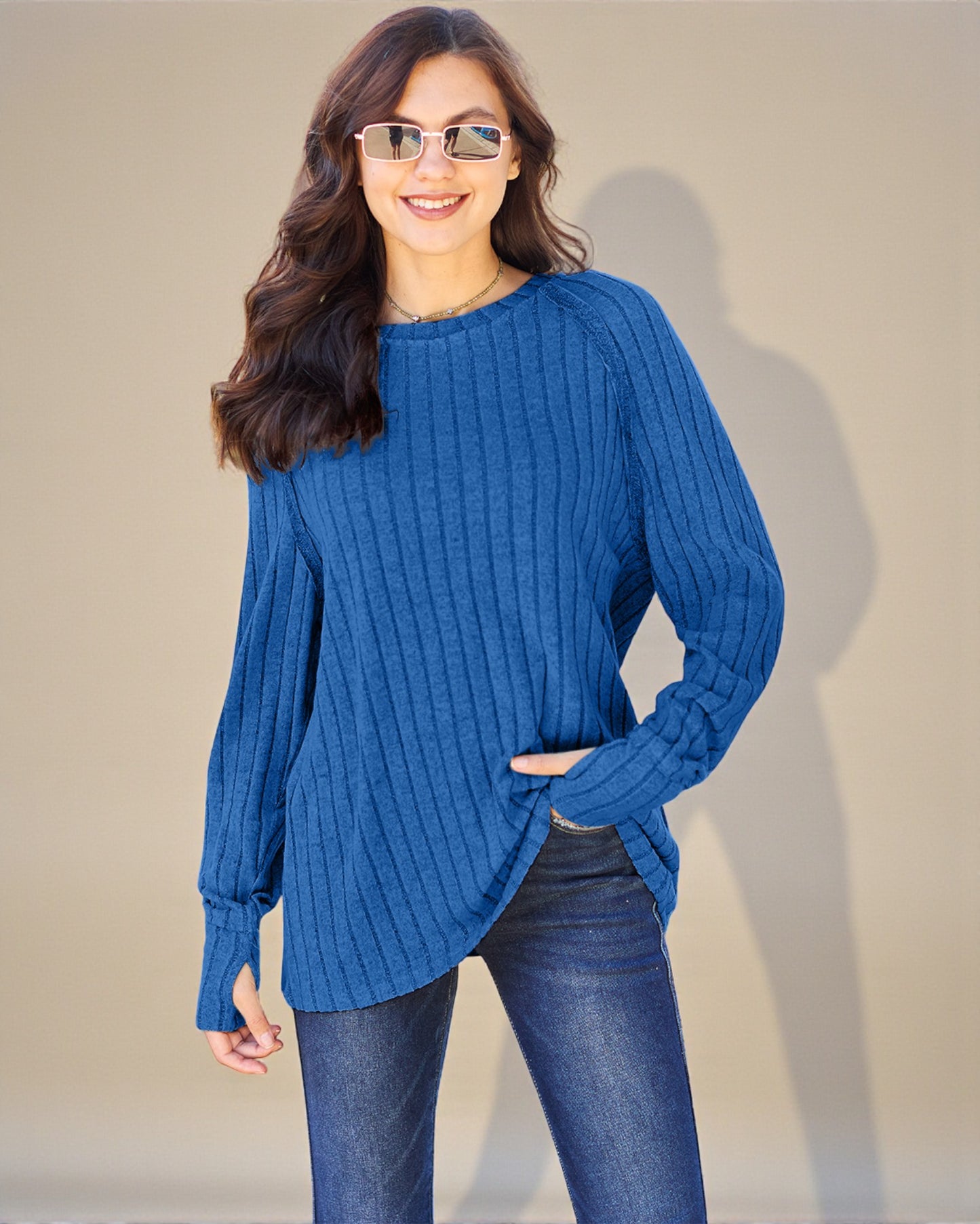 Woman wearing a blue sweater and sunglasses against a plain background