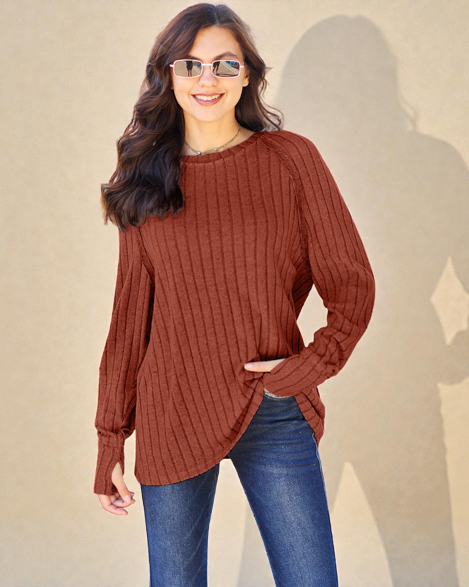 Woman wearing a brown ribbed sweater and blue jeans against a beige background