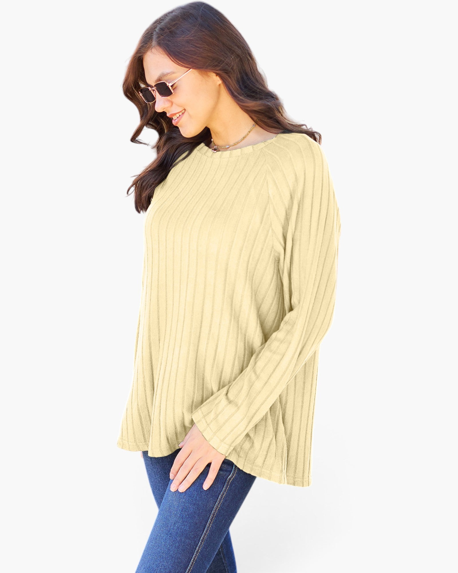 A woman wearing a pale yellow ribbed knit long-sleeve top and blue jeans, photographed against a plain light gray background.
