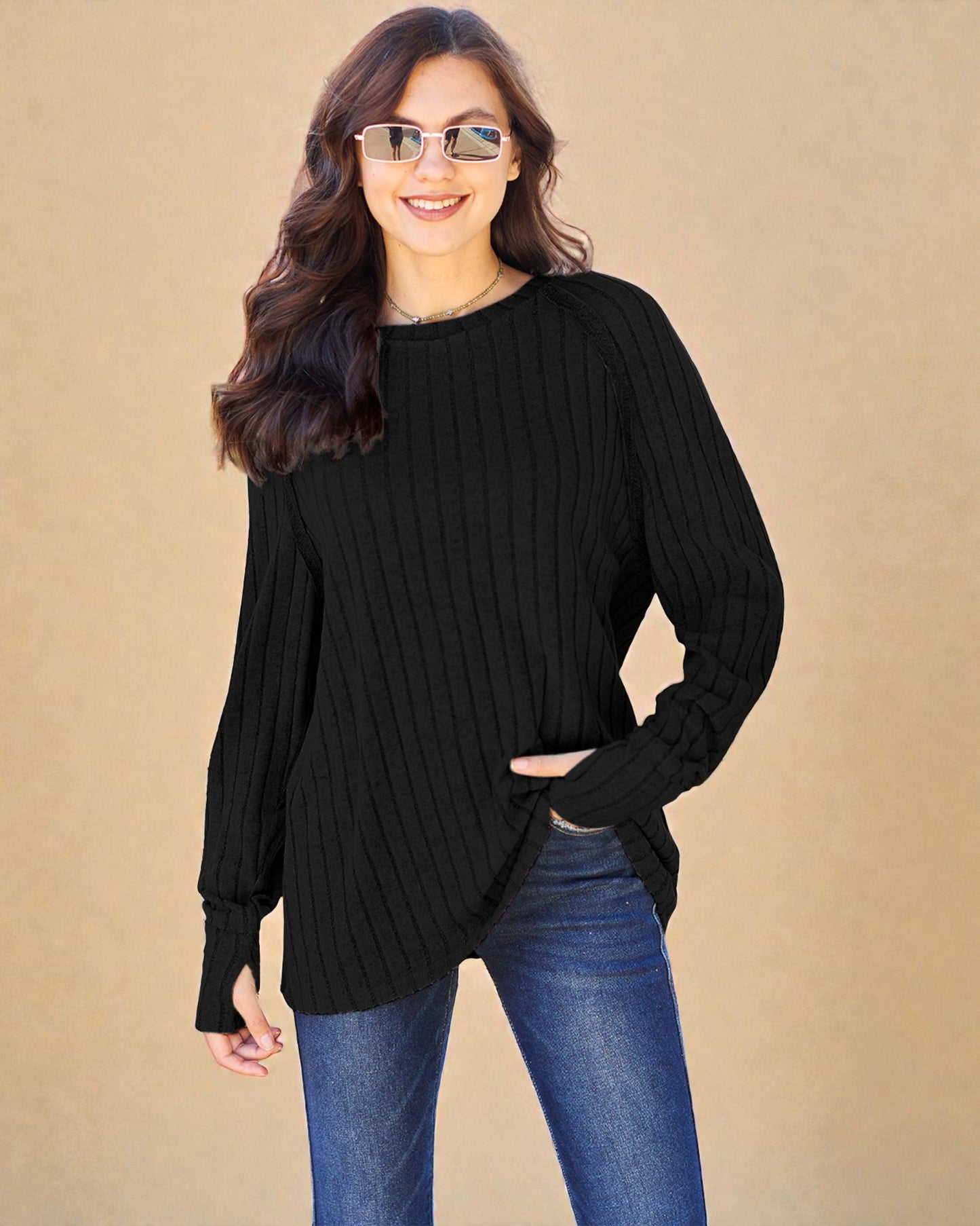 Woman wearing a black ribbed sweater and blue jeans against a beige background