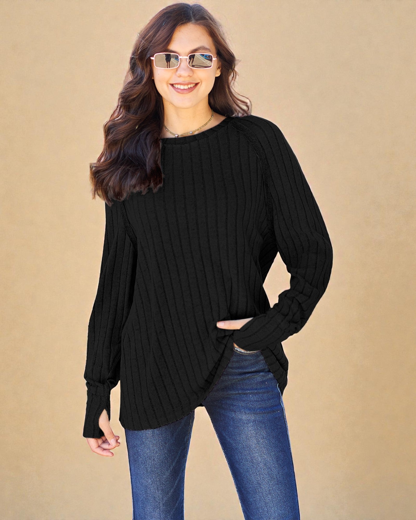 Woman wearing a black ribbed sweater and blue jeans against a beige background