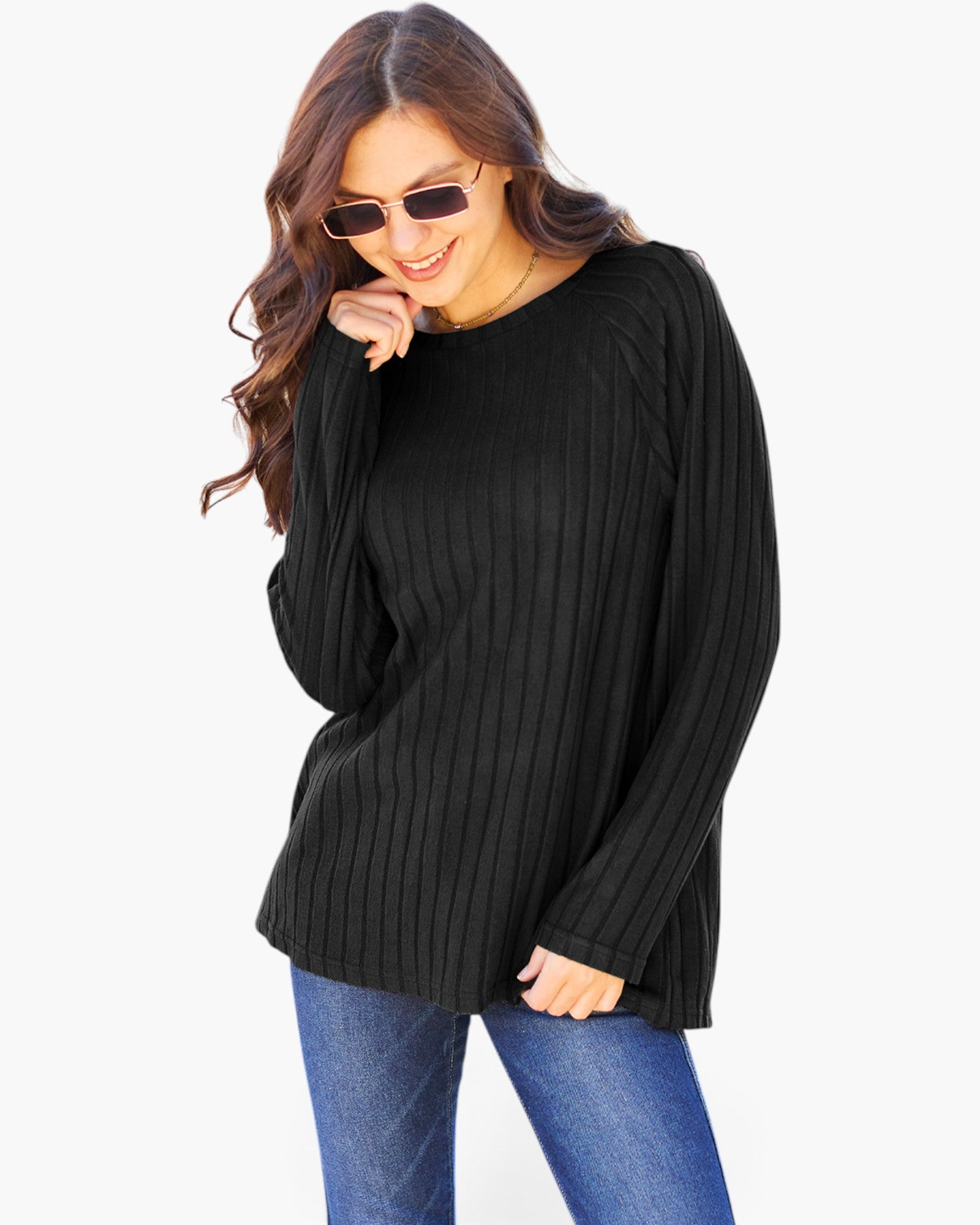 A woman wearing a black ribbed knit long-sleeve top and blue jeans, posing against a light gray background.