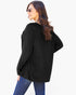 A woman wearing an oversized black ribbed knit top and blue jeans, photographed from the back against a plain white studio background.