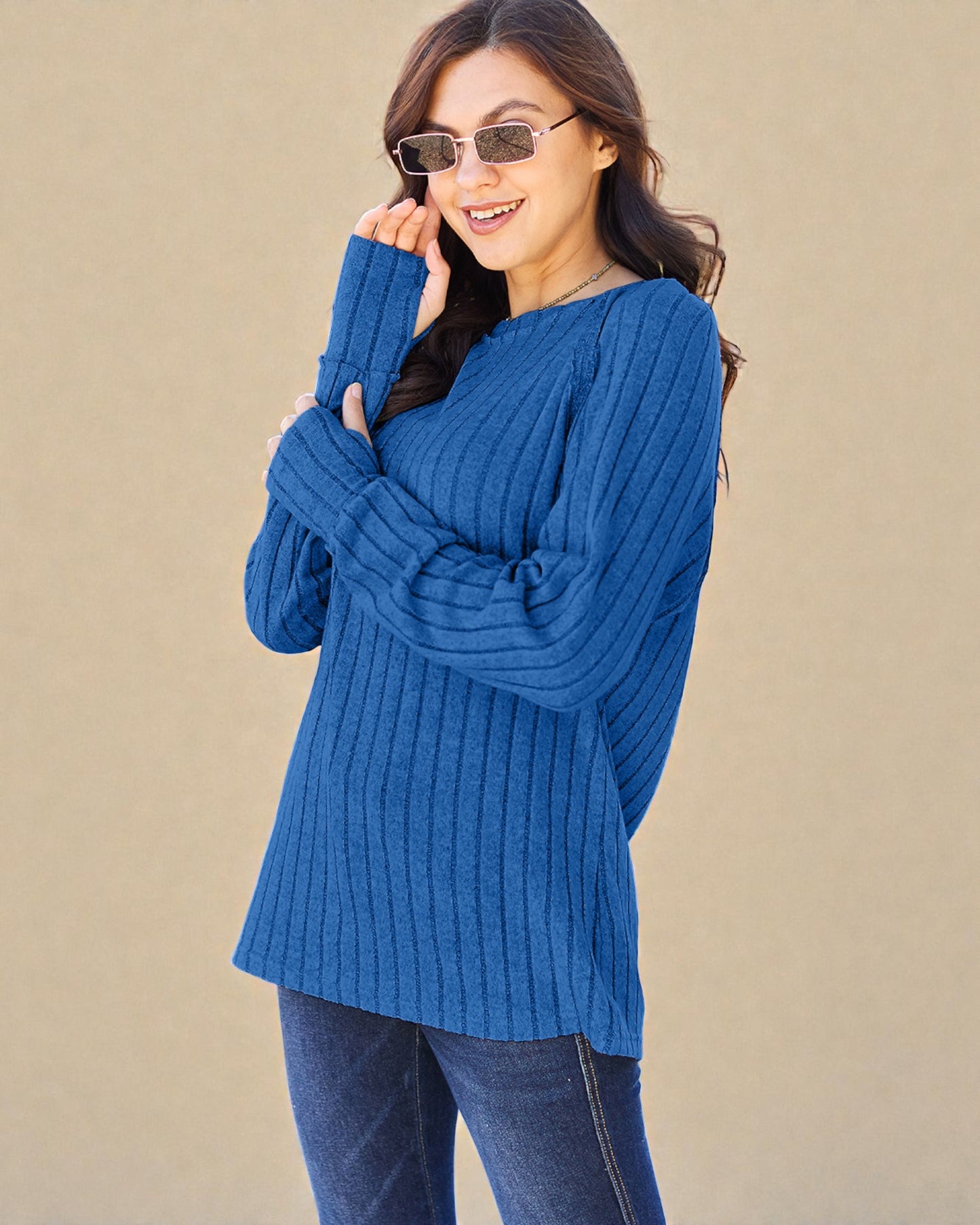 Woman wearing a blue sweater and sunglasses against a beige background