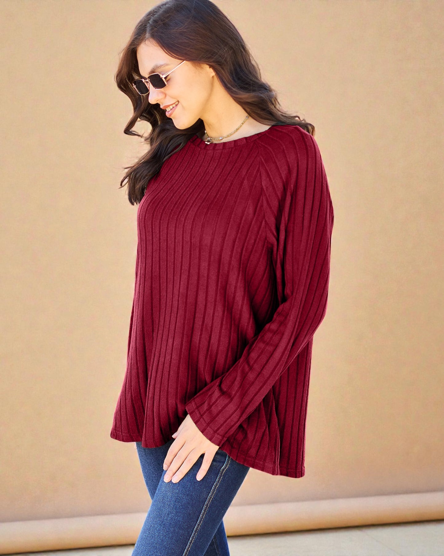 Woman wearing a burgundy ribbed sweater and sunglasses against a beige background