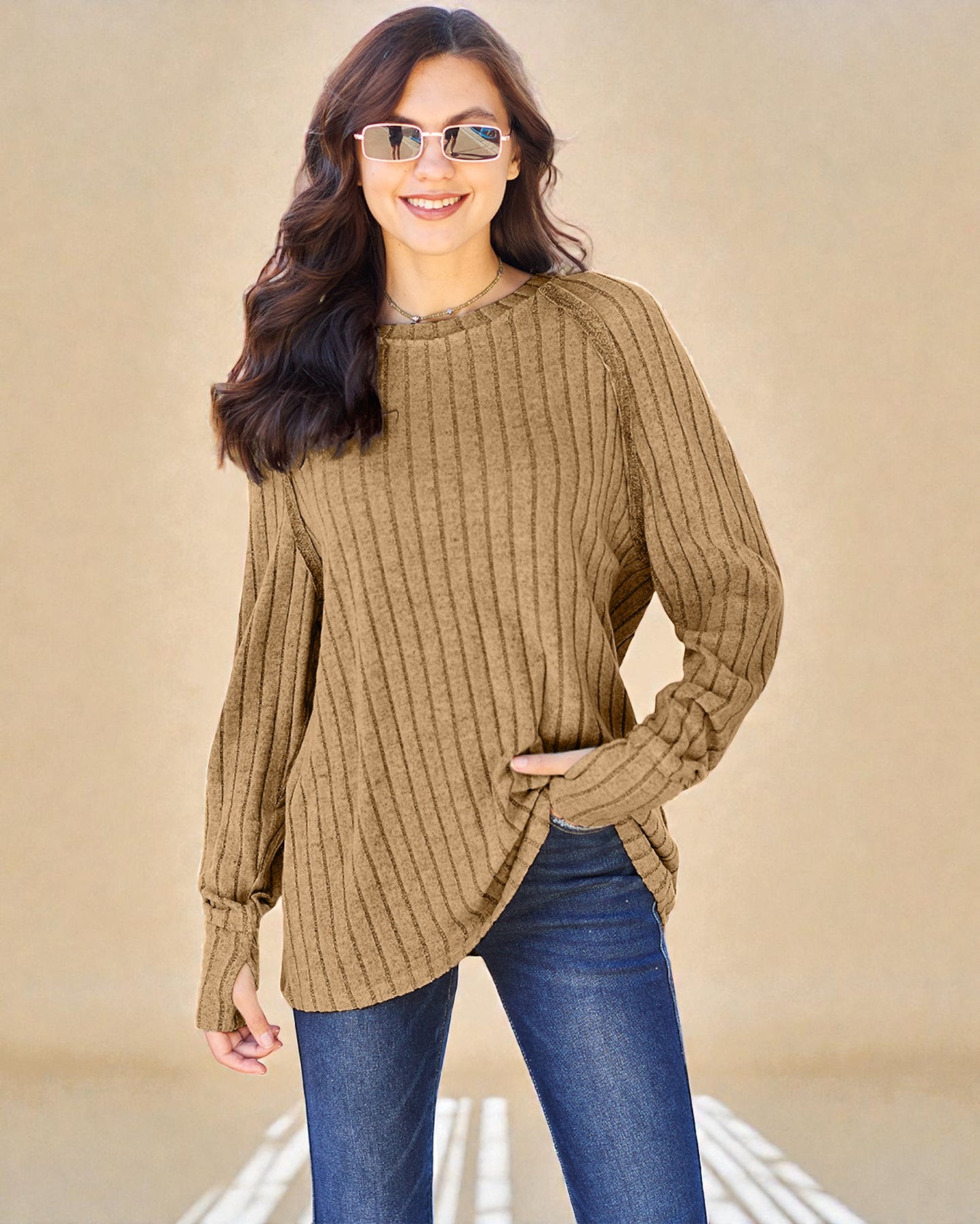 Woman wearing a brown ribbed sweater and blue jeans against a beige background