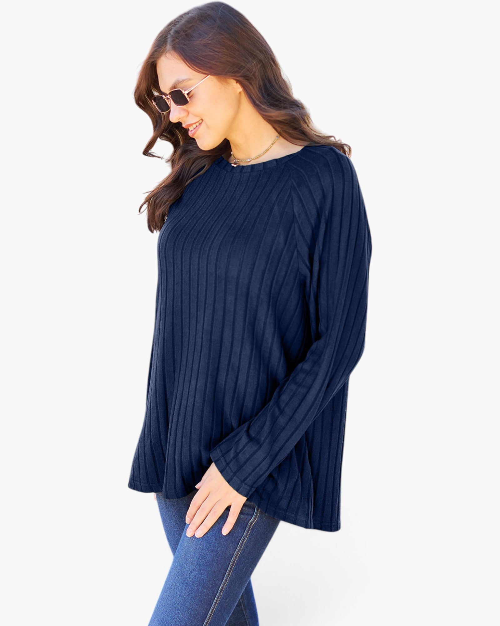 A woman wearing a navy blue ribbed knit long-sleeve top and blue jeans, photographed against a plain light background.