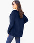 A woman wearing a navy blue ribbed knit long-sleeve sweater and blue jeans, photographed from the back against a plain white studio background.