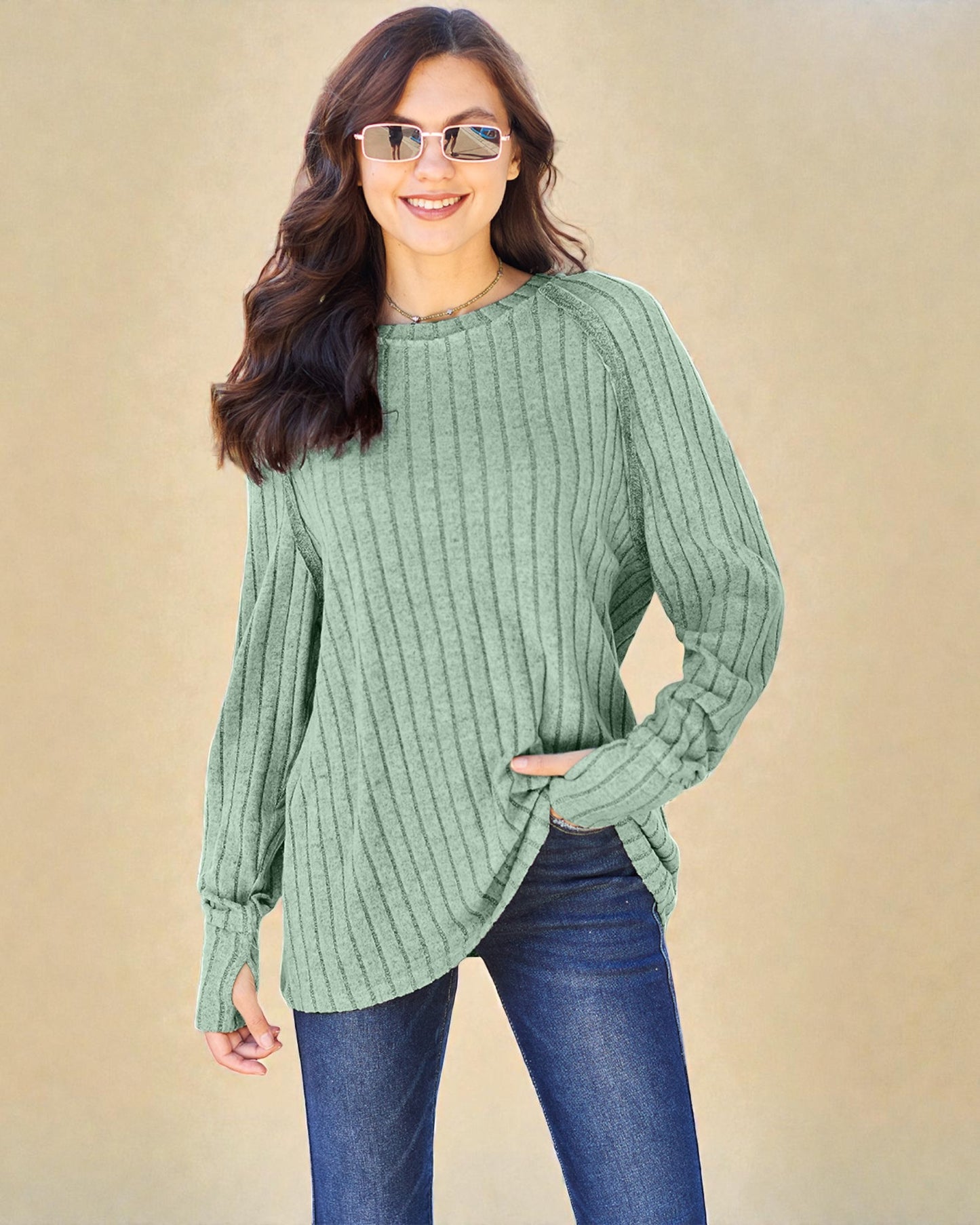 Woman wearing a green ribbed sweater and blue jeans against a beige background