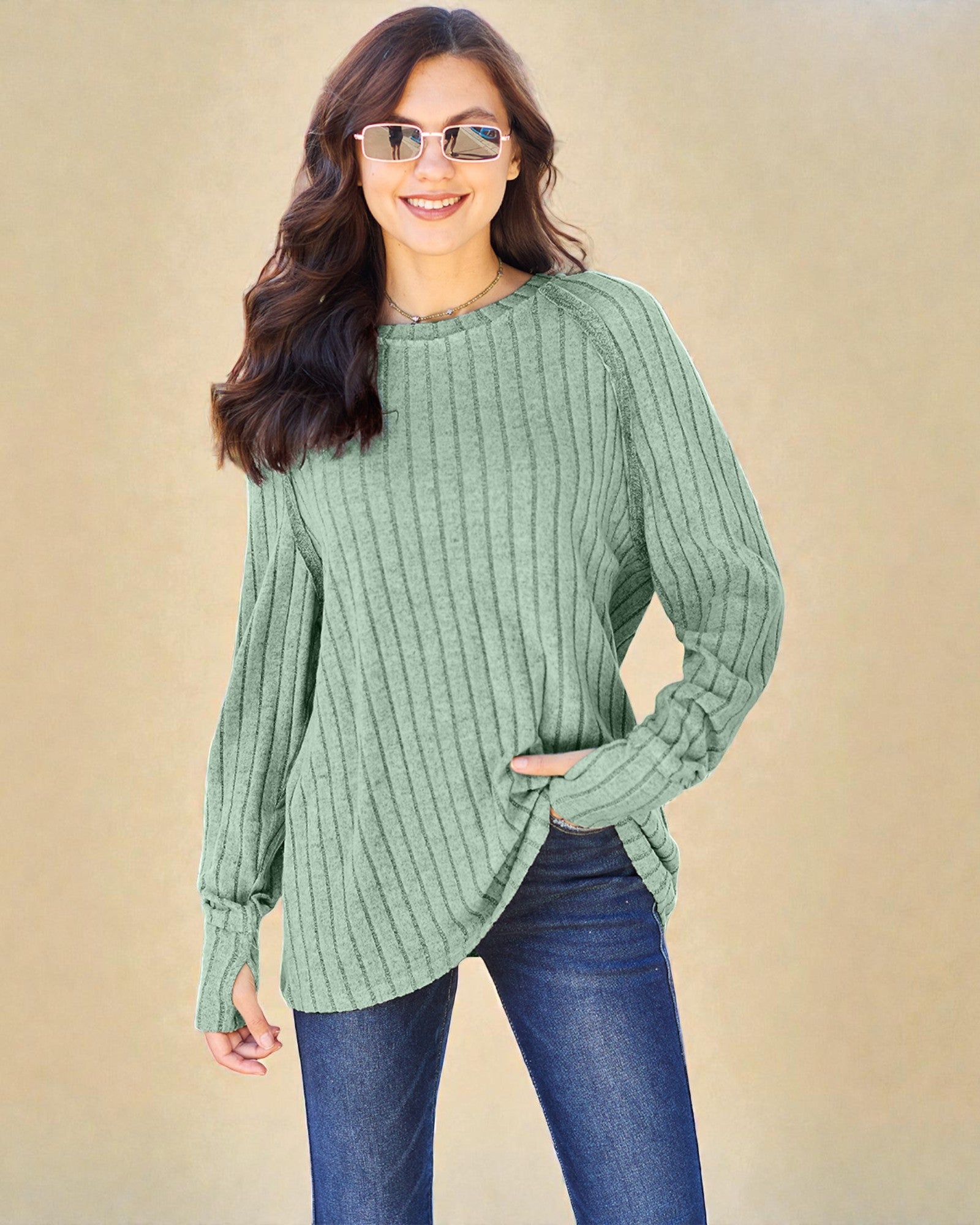 Woman wearing a green ribbed sweater and blue jeans against a beige background
