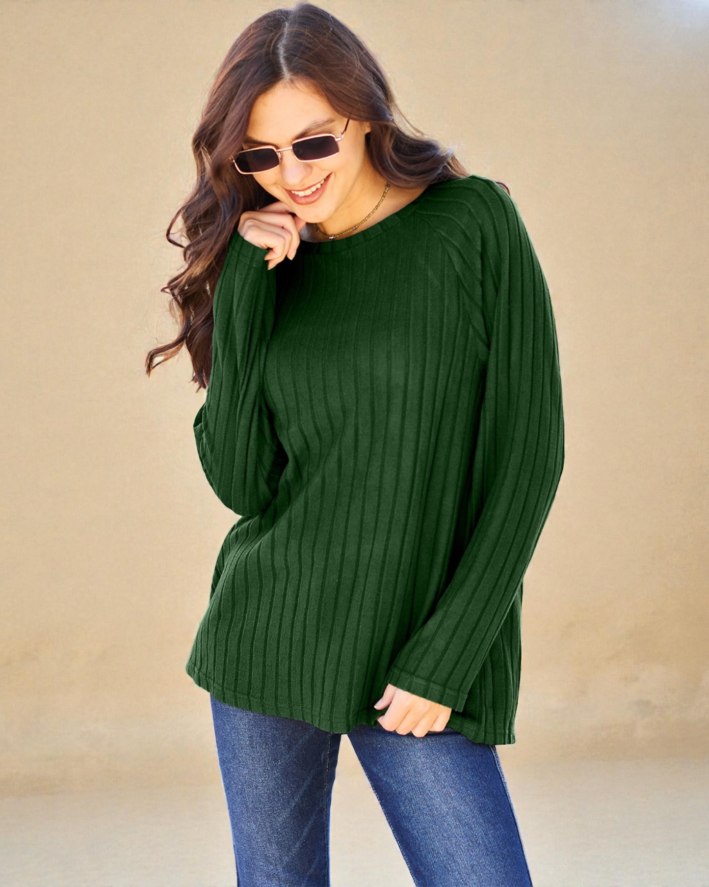 Woman wearing a green sweater and blue jeans against a beige background