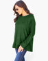 A woman wearing a dark green ribbed knit long-sleeve top and blue jeans, photographed against a plain light gray studio background.