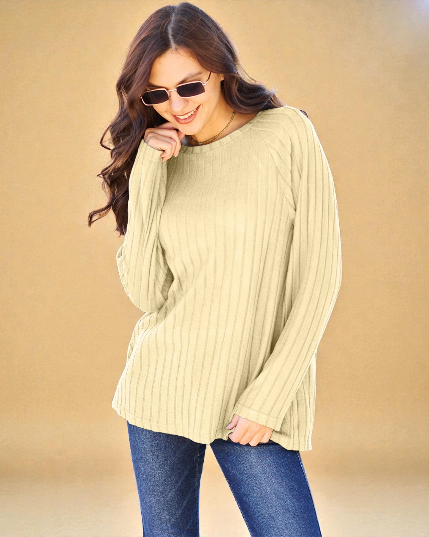 Woman wearing a light green ribbed sweater and blue jeans against a beige background