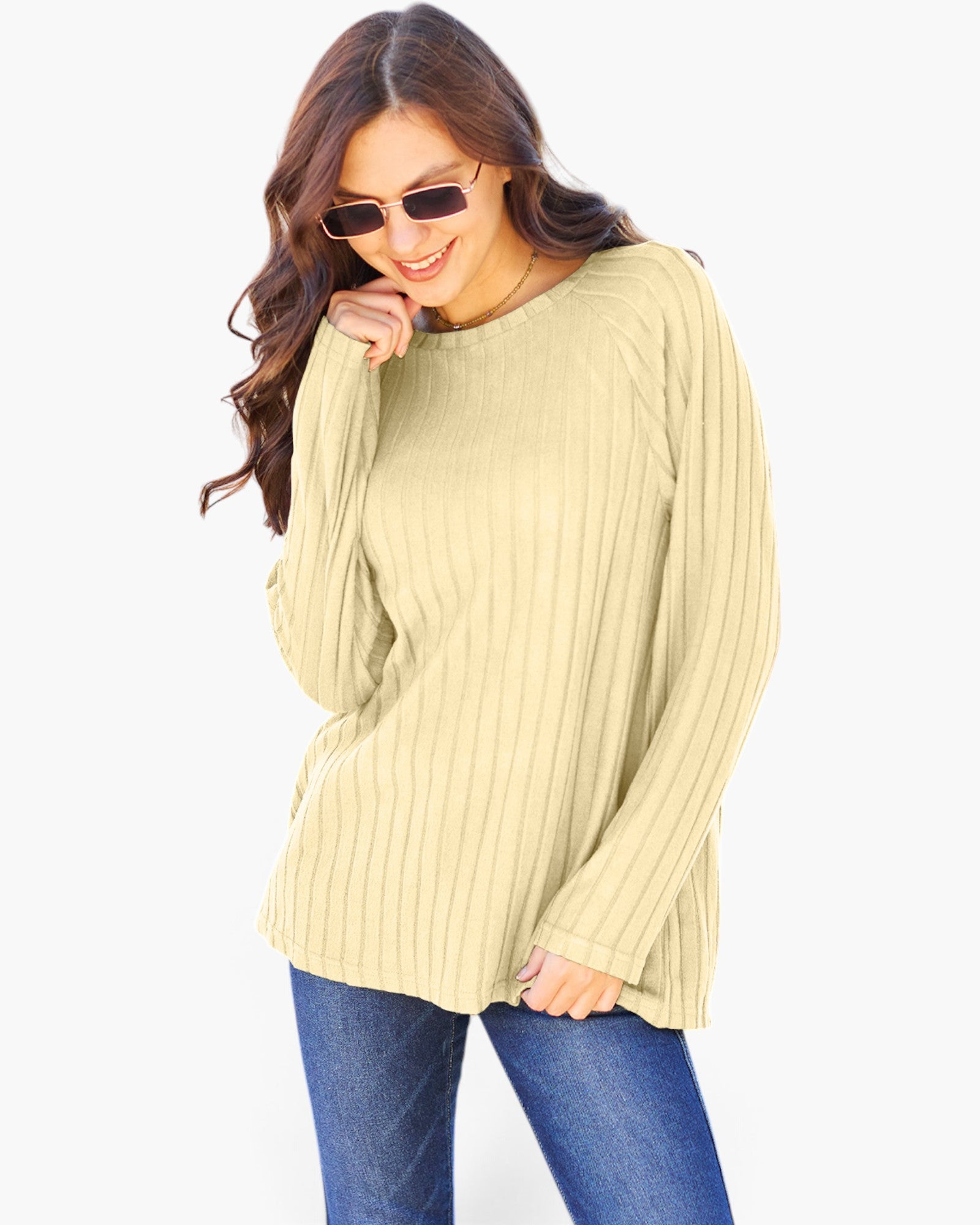 A woman wearing a light yellow ribbed knit long-sleeve top and blue jeans, posing against a plain white background.