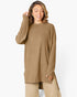 A woman wearing a ribbed knit long-sleeve tunic sweater in a warm camel brown color, paired with matching beige pants, against a plain white studio background.