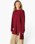 A woman wearing a ribbed knit long-sleeve tunic top in deep burgundy with a high-low hem and side slit, paired with beige pants, against a plain white studio background.